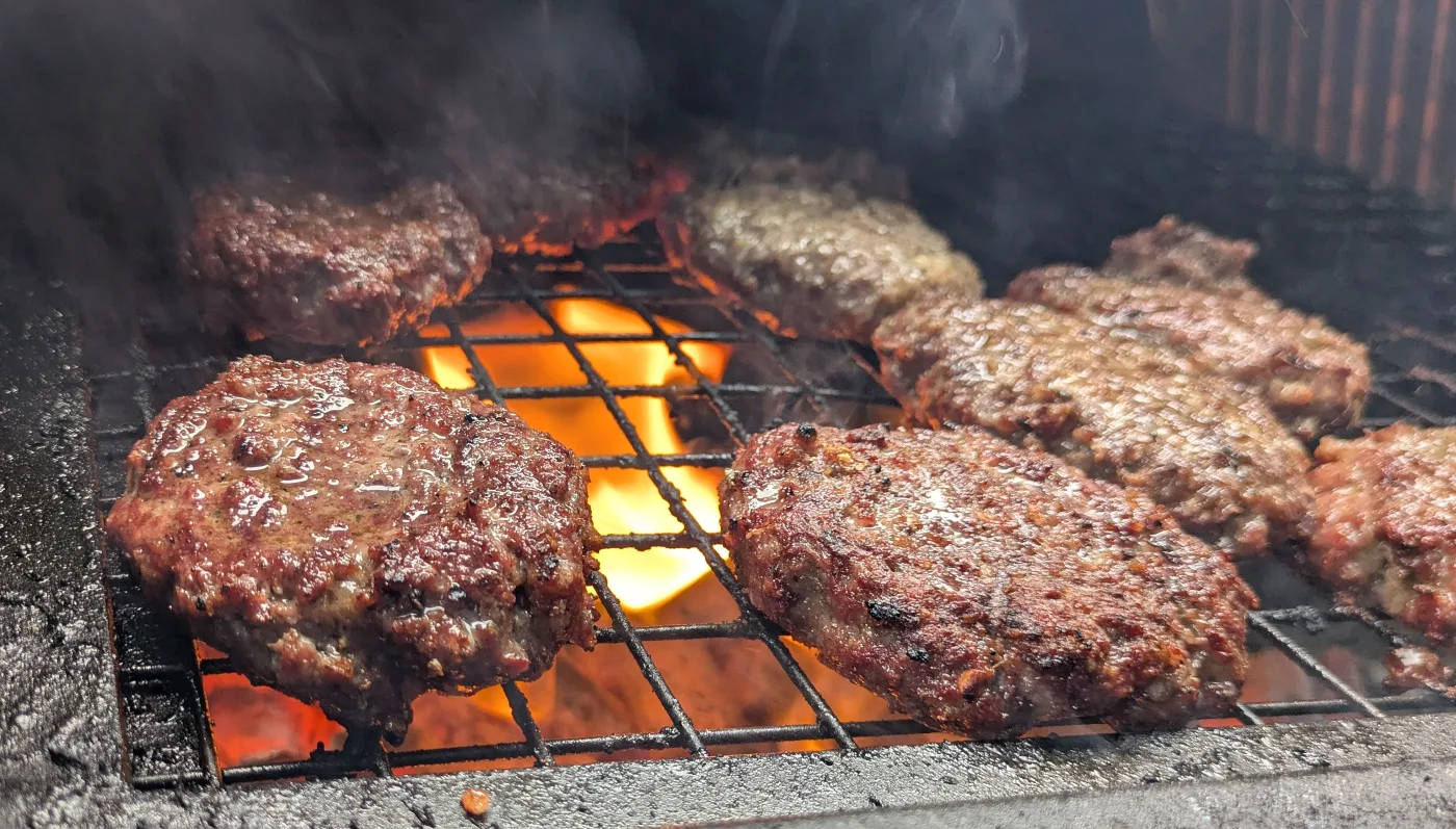 Burgers cooking over open flames on a charcoal BBQ